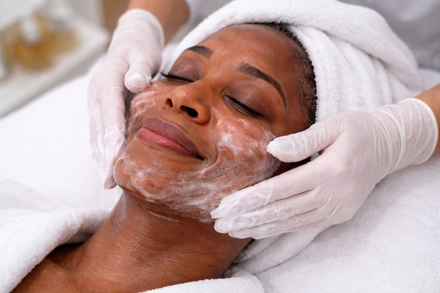 person receiving a professional facial treatment, with an esthetician gently cleansing her skin as she relaxes on a spa bed
